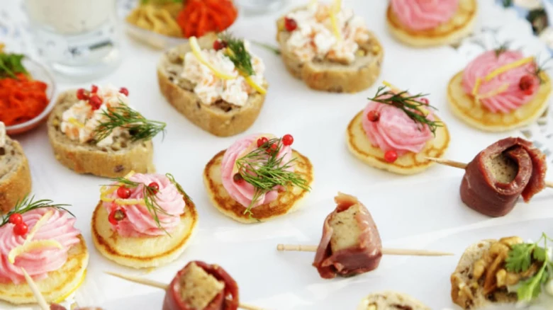 Různé slané pohoštění na párty: kanapky, mini palačinky s růžovou omáčkou a špekové rolády