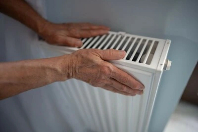 Starší ruce upravují ventilaci na topném tělese pro sezónu.