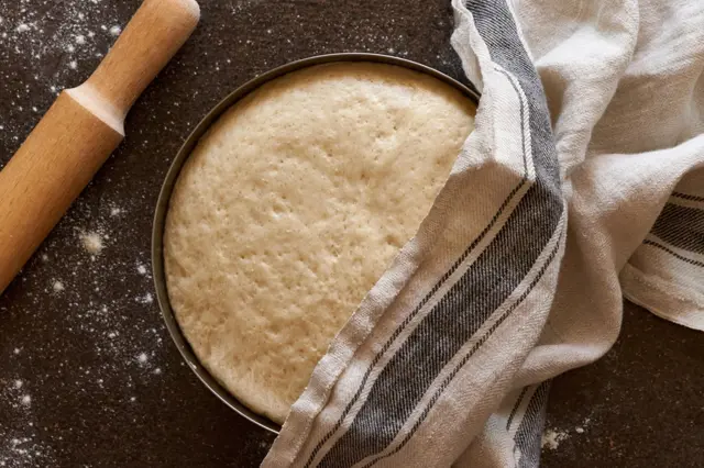 Zvýšené těsto v plechovém nádobí s kuchyňskou utěrkou