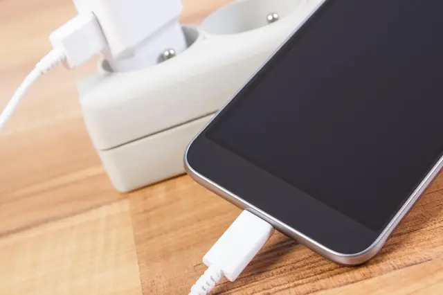 Mobilní telefon nabíjený bílou nabíječkou na dřevěné ploše.