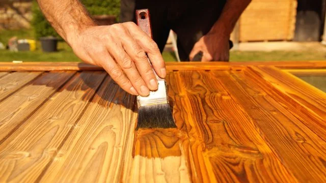 Nanášení laku na dřevo štětcem při renovaci dveří.