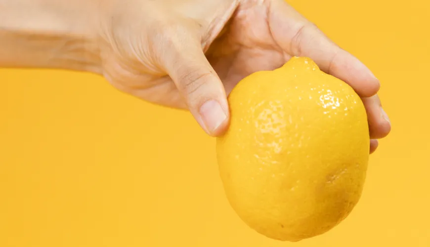 Ruka drží citron na žlutém pozadí