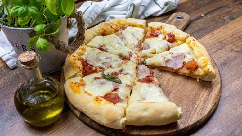 Pečená pizza na dřevěném podnosu s olivovým olejem a bazalkou