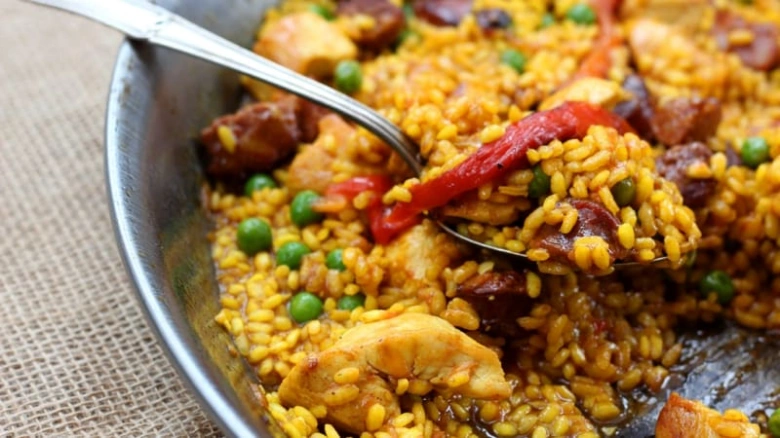 Španělská paella s kuřecím masem, hráškem a paprikou v kovovém nádobí
