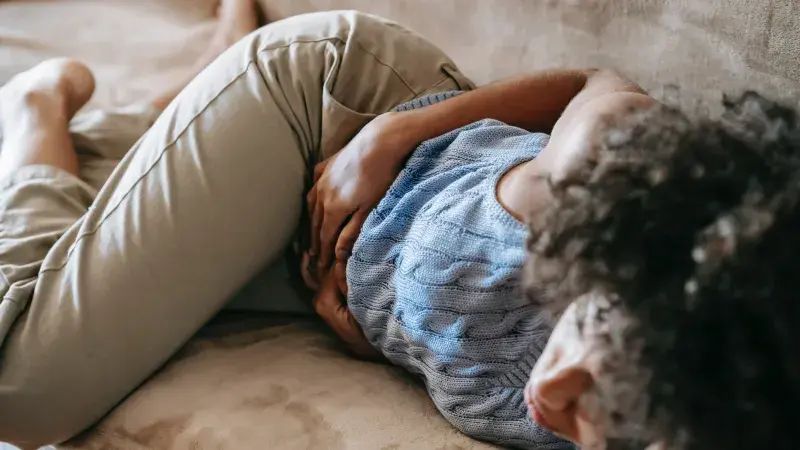 Osoba ležící na posteli s bolestí břicha