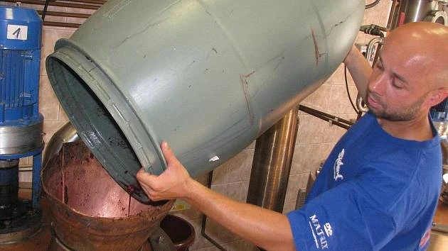 Muž přelévá kvas z nádoby do měděného sudu