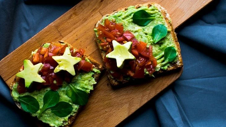 Avokádový toast s rajčaty a listy na dřevěné desce