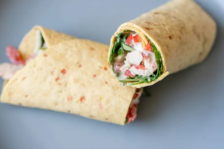Plněná tortilla s kuřecím salátem na modrém talíři.