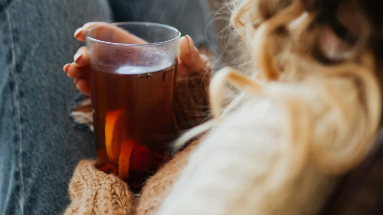 Osoba drží sklenici horkého bylinného čaje s pomerančem