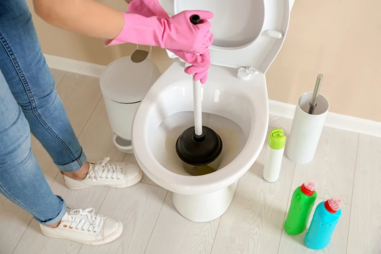 Osoba s růžovými rukavicemi čistí záchod kbelíkem