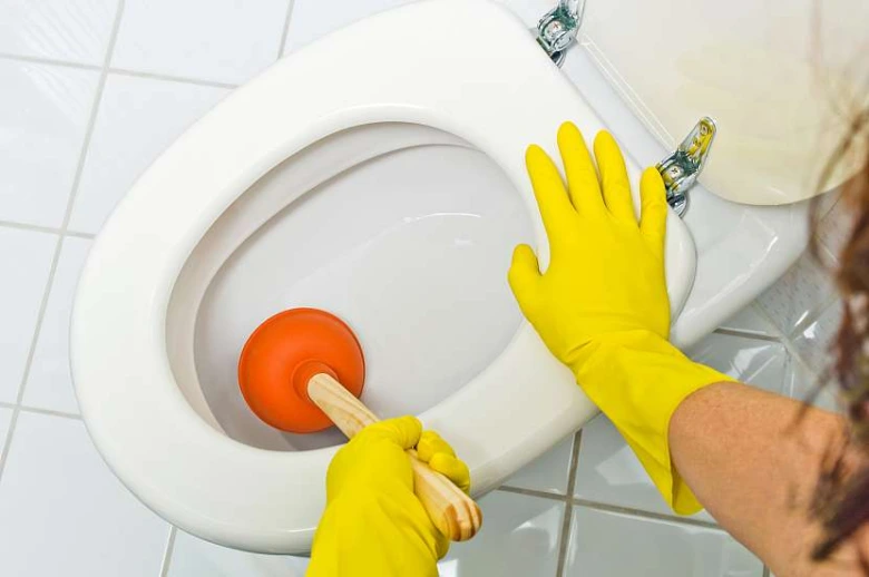 Osoba s žlutými rukavicemi čistí záchod kbelíkem