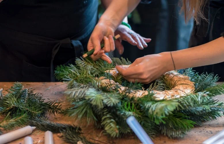 Ruce vyrábějí adventní věnec z jehličí a provázku