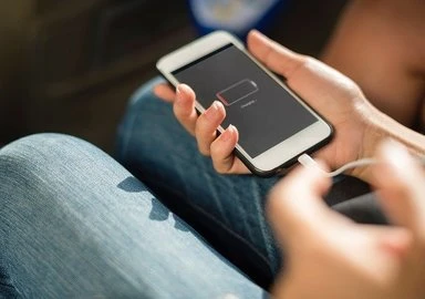 Člověk nabíjí mobilní telefon kabelovým adaptérem.