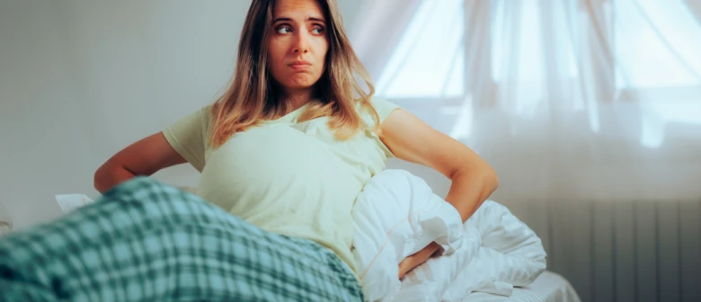 Těhotná žena v posteli, unavená a s bolestí v zádech