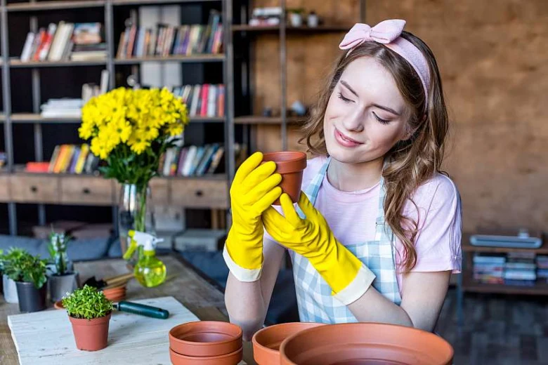 Žena s rukavicemi pečuje o pokojové rostliny v domácím prostředí
