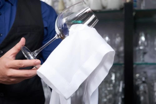 Číšník čistí sklenici vína bílým utěrkou v restauraci.