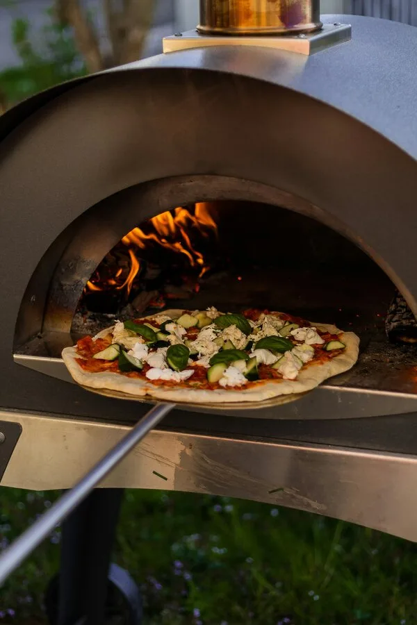 Pizzová pec venku s hořícím dřevem a pečenou pizzou