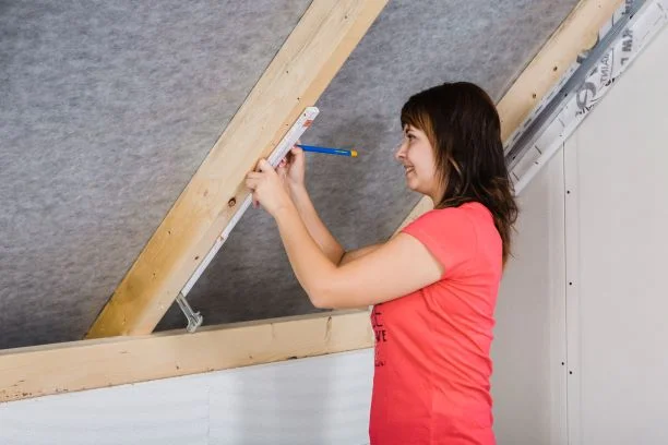 Žena měří a značí dřevěné trámy v podkroví před instalací sádrokartonu