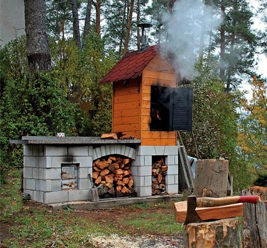 Dřevěná udírna s kameny, dřívím a kouřem v lese