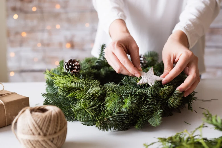 Ruce vyrábějí adventní věnec z jehličí s hvězdou a borovicovými šiškami