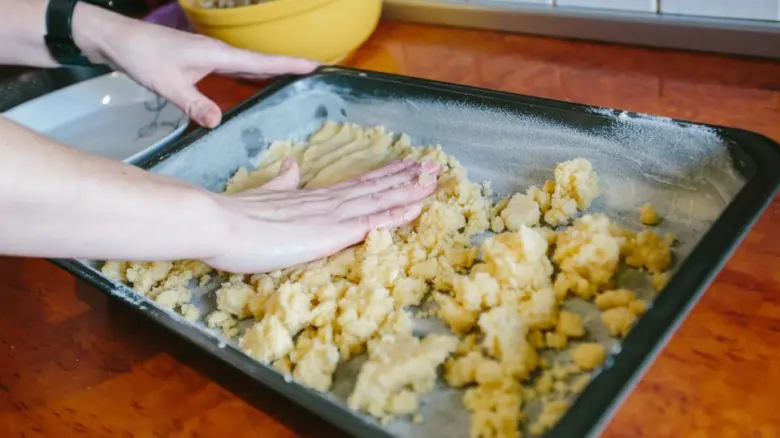 Ruce tlačí drobenkovou mouku do pekárenské formy