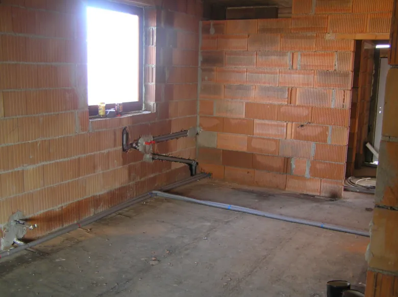 Stavební práce přístavby domu s cihlovými stěnami a instalací potrubí