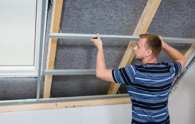 Muž instaluje kovový rastr pro sádrokarton v podkroví