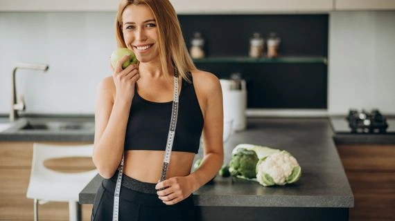 Žena s jablkem a měřítkem v kuchyni, zdravá strava
