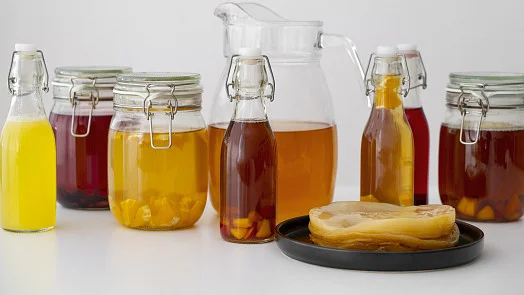 Různé lahve s kombuchou a SCOBY na talíři
