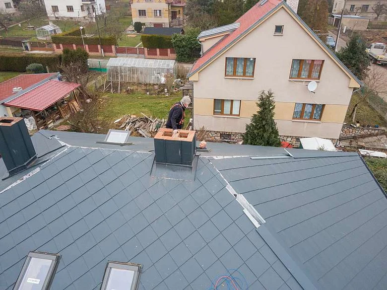 Muž instaluje oplechování komína na střeše.