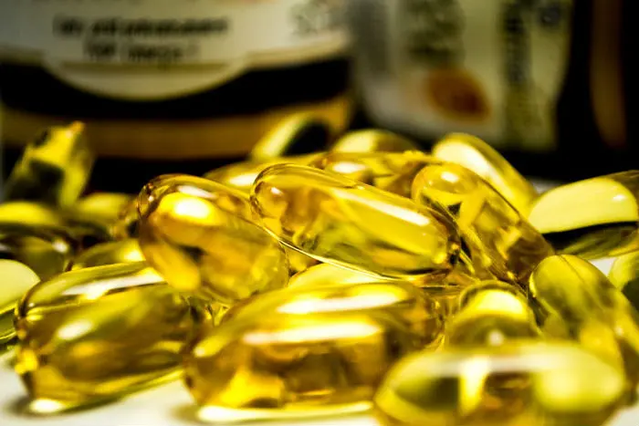 Zlaté kapsle omega-3 mastných kyselin na bílém podkladu.