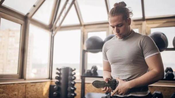Muž v posilovně připoutává popruhy svých sportovních bot.