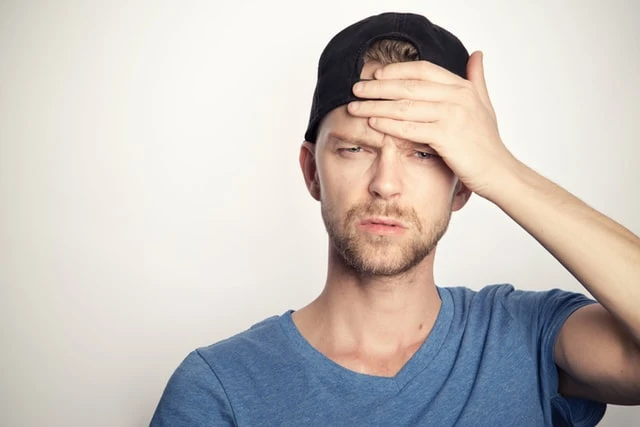 Muž s rukou na čele, vyjadřující bolest hlavy.