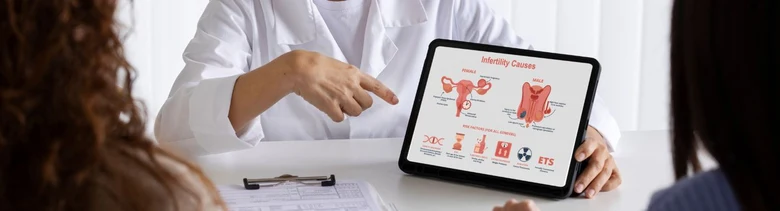 Lékař ukazuje pacientům infografiku o příčinách neplodnosti na tabletu.