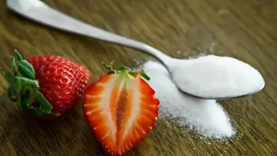 Čerstvé jahody a lžíce cukru na dřevěném povrchu.