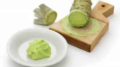 Čerstvý kořen wasabi se tře na dřevěné desce do zelené pasty.