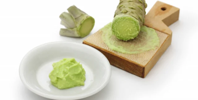 Čerstvý kořen wasabi se tře na dřevěné desce do zelené pasty.
