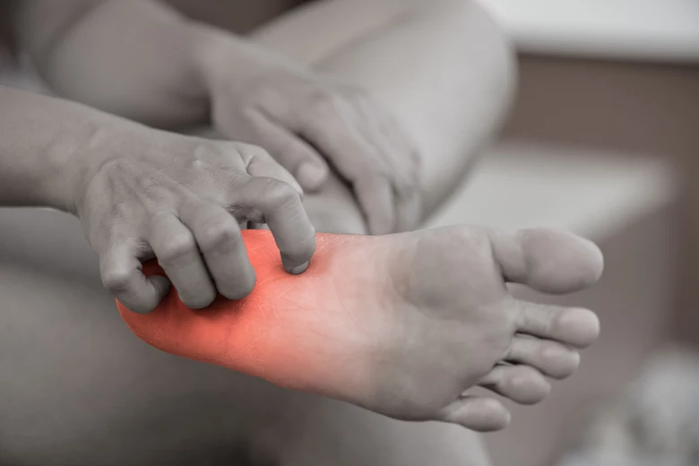 Člověk drží nohu s červeným zvýrazněním bolesti neuropatie.
