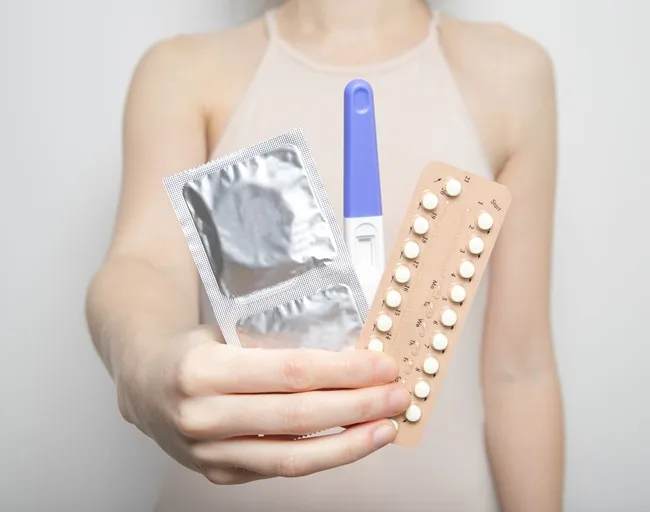 Ruce drží kondom, antikoncepční pilulky a těhotenský test.