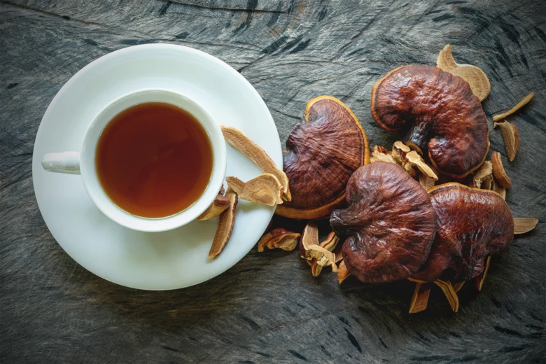 Sušené houby reishi vedle šálku čaje na dřevěném povrchu.