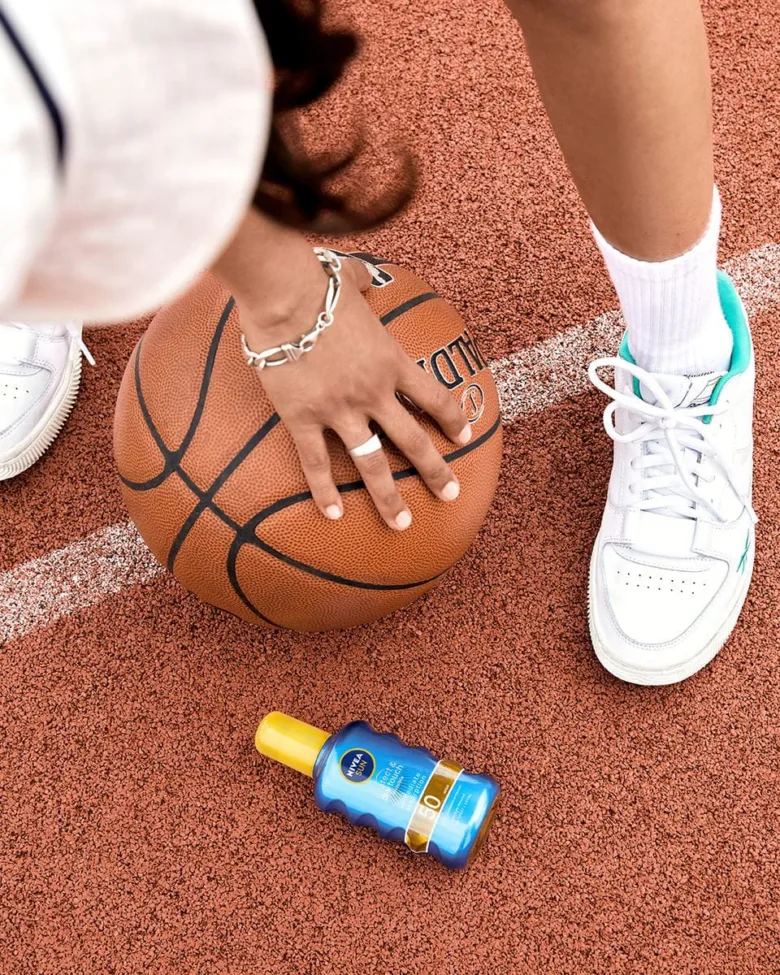 Ručník s basketbalovou míčkou a fľaškou opaľovacieho krému na dvore.