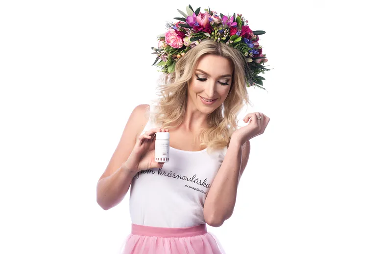 Žena s květinovou korunou drží lahvičku doplňků stravy pro vlasy.