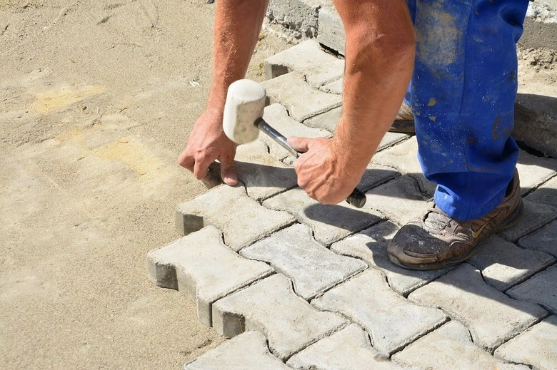 Ruční pokládka zámkové dlažby kladivem do betonu.