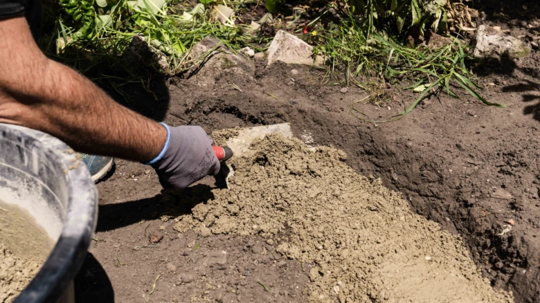 Muž míchá beton ručně v zahradě pro stavbu ohniště.