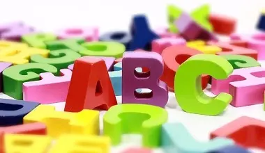 Kolorované plastické písmena ABC rozsypaná na bílém povrchu.