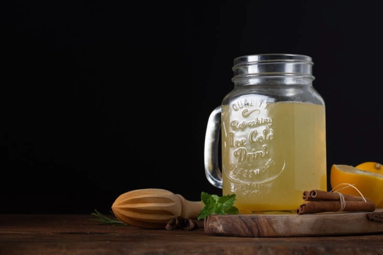 Sklenice s citronovým nápojem, hřebíčkem a kořením na tmavém pozadí.