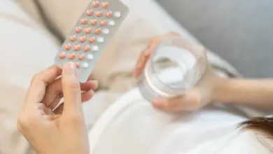 Žena drží tablety antikoncepce a sklenici vody.