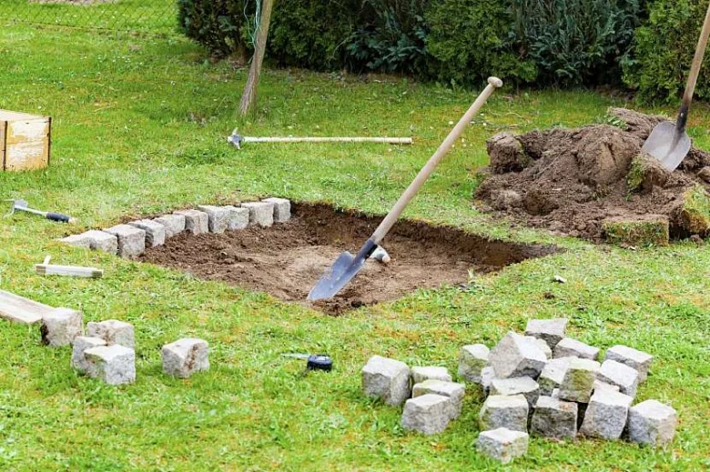 Stavba kamenného ohniště s nástroji na trávníku.