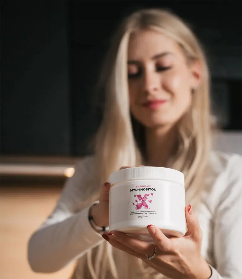 Žena drží bílý nádobek s myoinositolem v rukou.