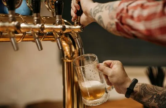 Člověk nalévá pivo z kohoutku do sklenice.